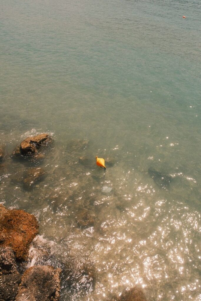 A bright yellow buoy floating in clear, sunlit water near rocky shorelines.